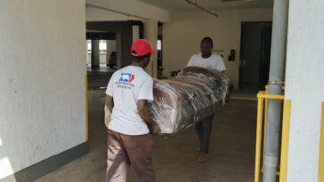 Professional Nairobi movers carefully carrying a plastic-wrapped sofa during a residential move.