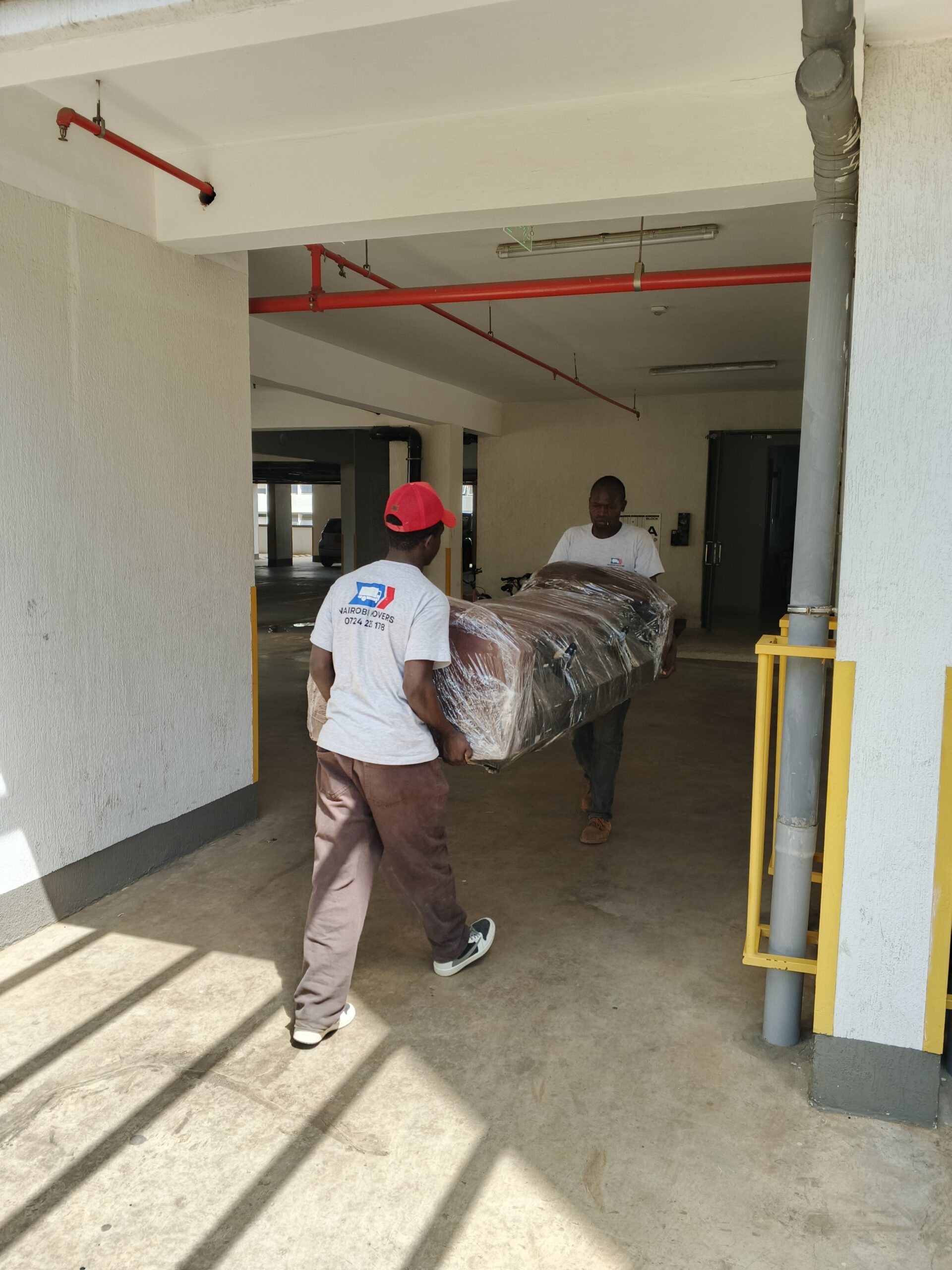 Professional Nairobi movers carefully carrying a plastic-wrapped sofa during a residential move.